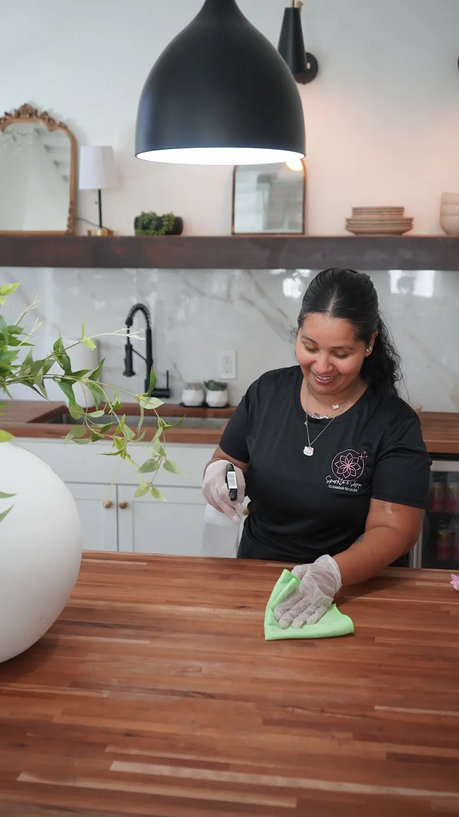Smiling Sparkle & Shine cleaner wiping a kitchen countertop in a bright home